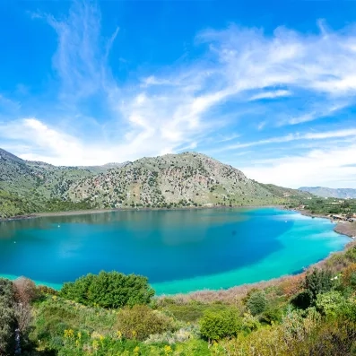 Lac de Kournas en Crète, eau turquoise entourée de collines verdoyantes et montagnes, paysage naturel paisible.