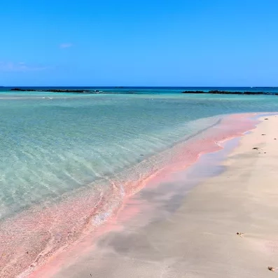 Plage d’Elafonissi en Crète avec sable rosé, eau turquoise peu profonde et lagon protégé, paysage paradisiaque.