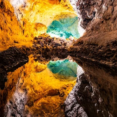 Intérieur de la Cueva de los Verdes à Lanzarote, grotte volcanique illuminée, reflets d’eau et formations de lave.