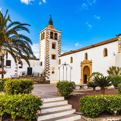 Église et place de Betancuria à Fuerteventura, village historique des Canaries, architecture blanche, palmiers et ciel bleu.