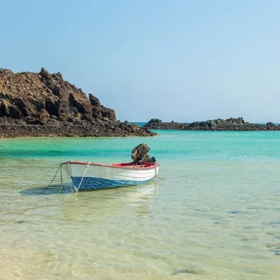 Petit bateau sur eau turquoise près de l’île de Lobos à Fuerteventura, lagon cristallin, rochers volcaniques et ciel clair.