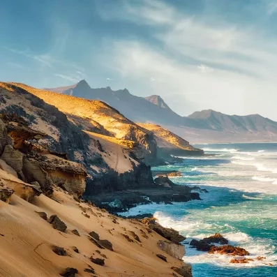 Côte sauvage du parc naturel de Jandía à Fuerteventura, falaises, plages dorées et océan Atlantique sous une lumière dorée.