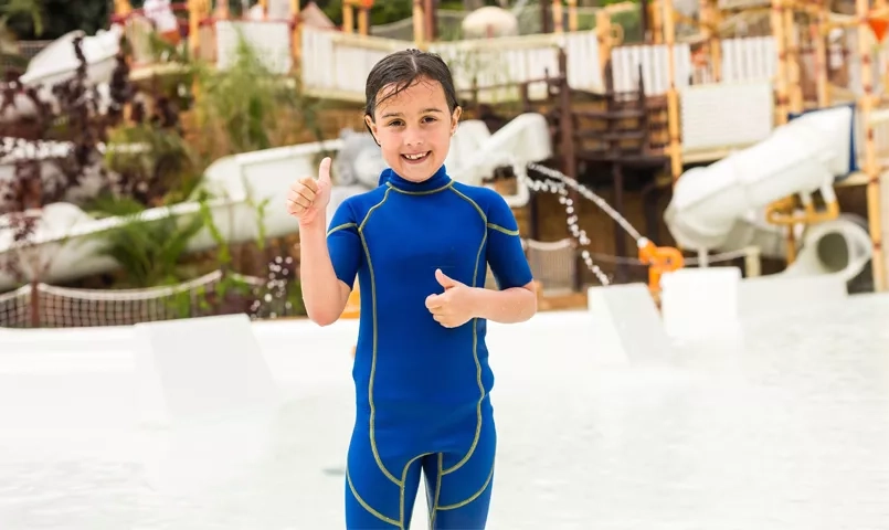 Enfant souriant dans un parc aquatique à Tenerife, toboggans et jeux d’eau en arrière-plan, activité idéale en famille aux Canaries.