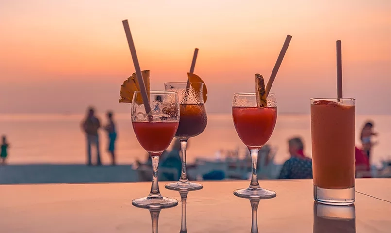 4 verres à cocktails sur une plage au soleil couchant