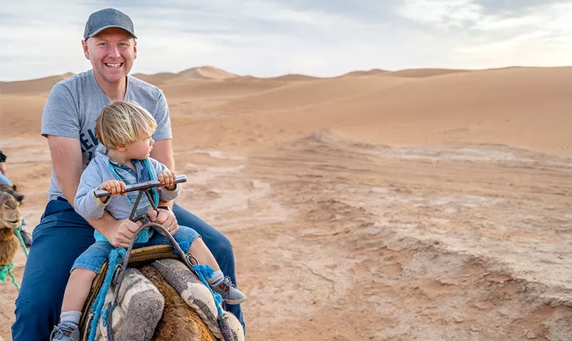 Un père et son fils sur un dromadaire sur les dunes dans le désert