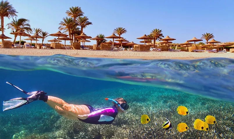 Femme faisant de la plongée sous l'eau et au loin la plage avec des parasols